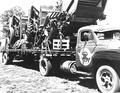 shows a AA series international truck with the single axle trailer loaded with three harvesters circa 1958